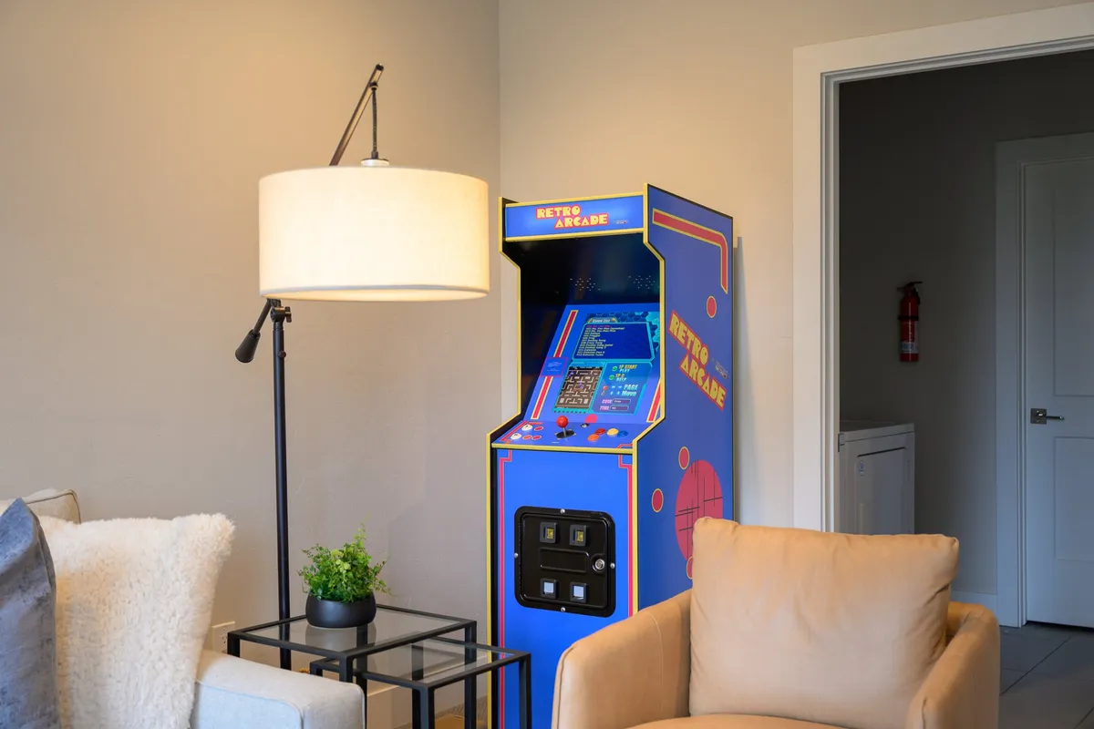 A retro arcade machine stands beside comfortable seating and a warm floor lamp. The layout encourages both gaming and relaxed conversation, providing a nostalgic atmosphere perfect for friendly competitions or unwinding after outdoor adventures.