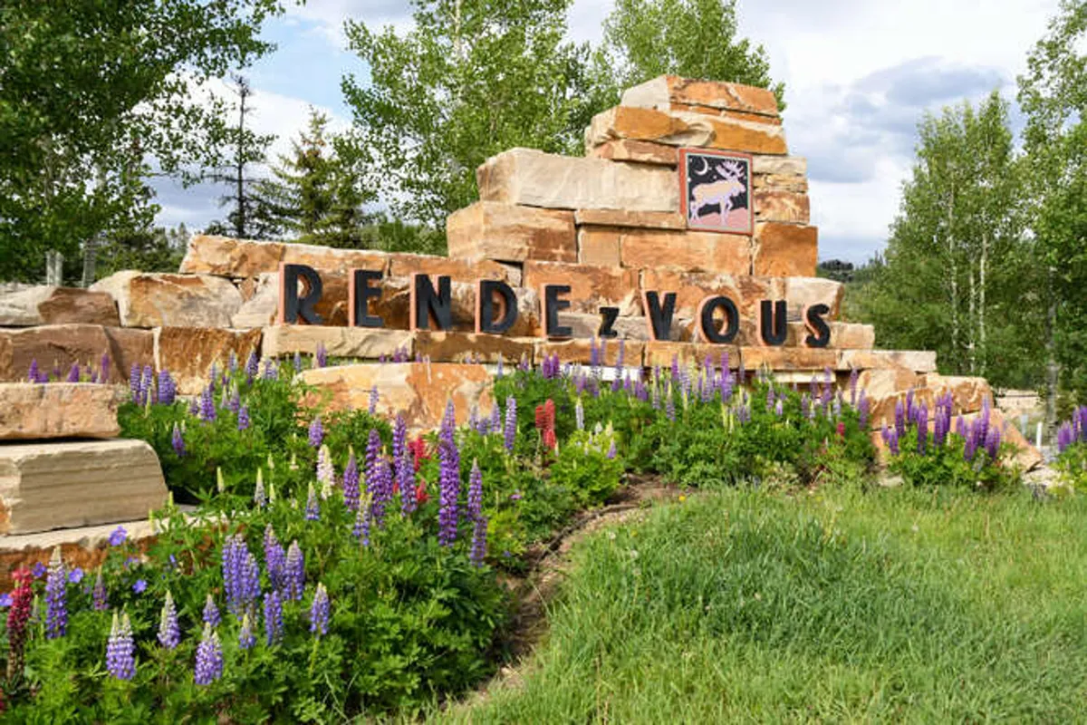 A rock formation adorned with signage and vibrant flower beds marks an entrance to a local nature area. The inviting landscaping and signage hint at nearby trails and opportunities for exploration, reinforcing the home’s connection to local attractions and the greater environment.