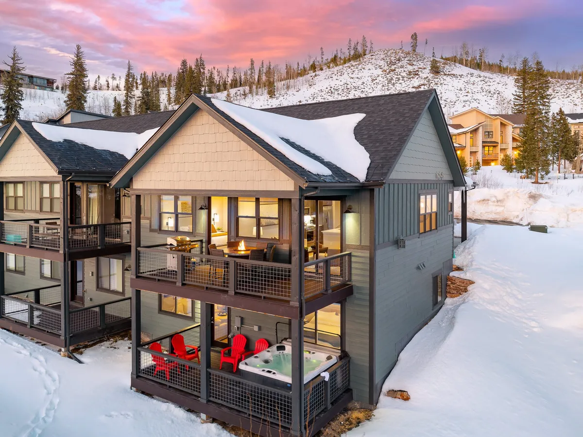 An inviting exterior shot of a wooden deck featuring a steaming hot tub, bright red chairs, and a beautiful snow-covered landscape. It conveys the perfect après-adventure setting for relaxation after active days spent outdoors.