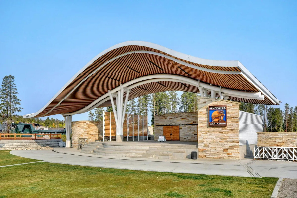 An outdoor stage with a distinctive curved roof structure and stone walls, providing a welcoming space for concerts and community events. The stage area is centrally located and suggests festive gatherings.