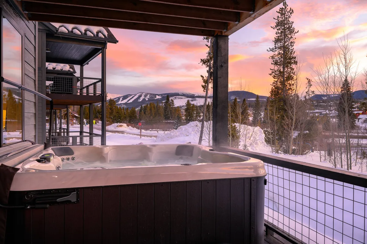 An inviting outdoor hot tub surrounded by natural beauty, with views of the mountains and a stunning sunset sky. The warm water and tranquil setting create the perfect environment for evening relaxation and stargazing.